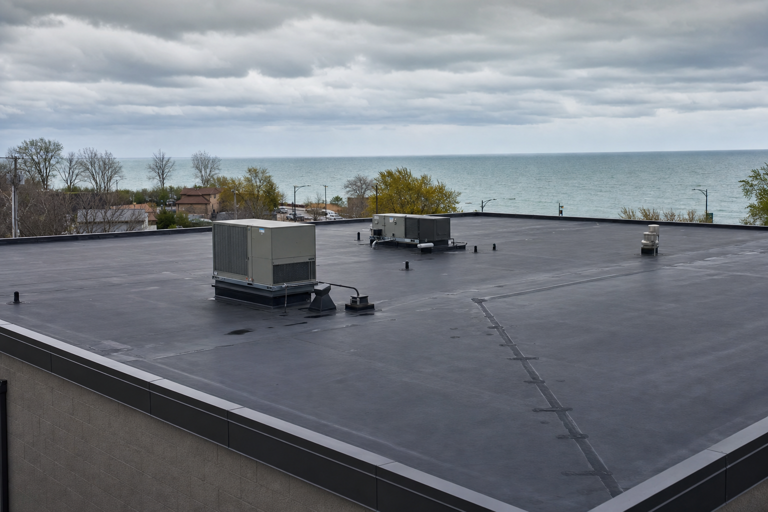 documentary photo of a dark EPDM rubber membrane roof on a small commercial building in Waukegan, visible rooftop units and clean drainage path, Lake Michigan moody gray sky, no people, no text on image