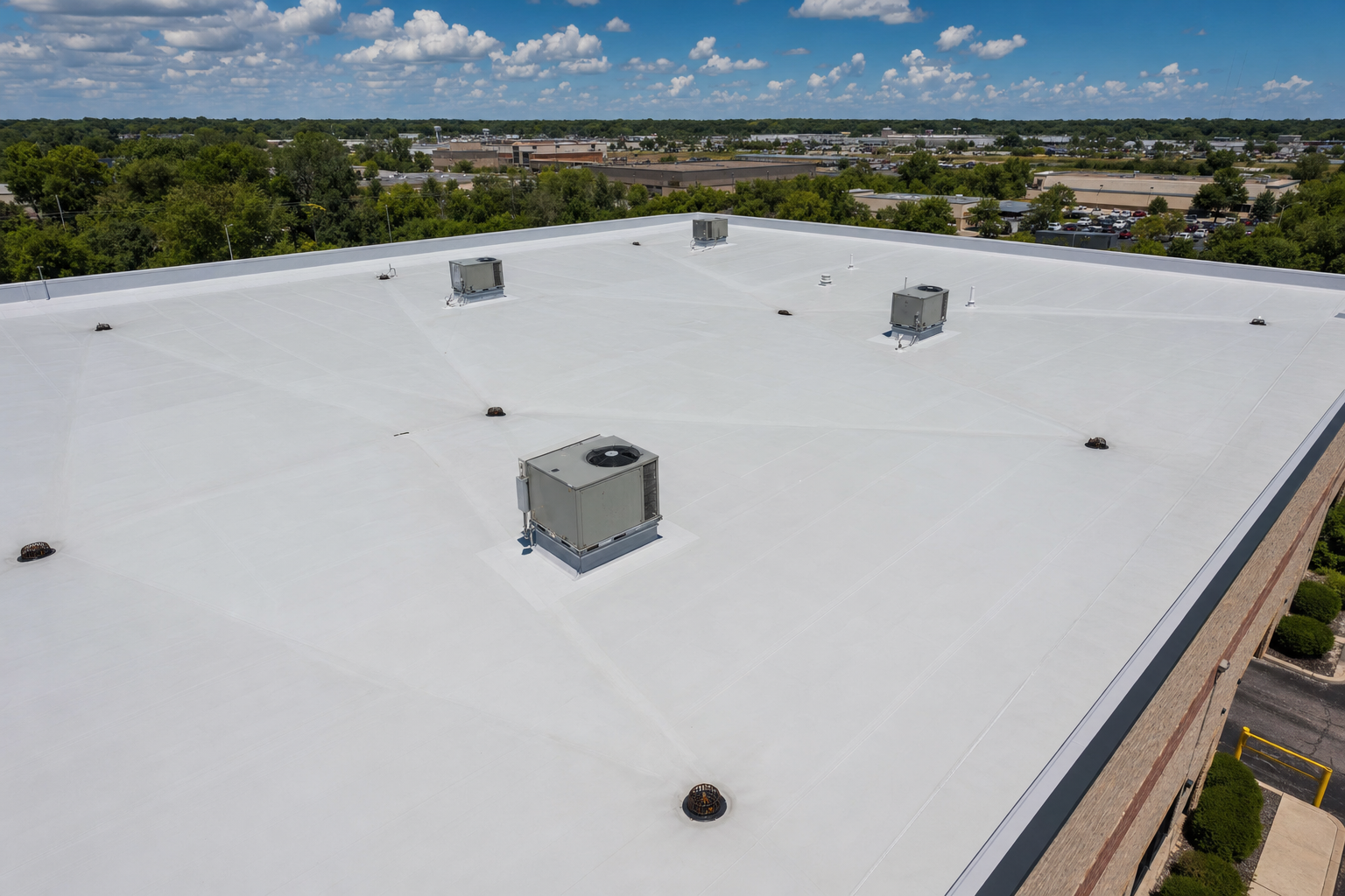 overhead drone-style photo of a clean commercial flat roof in Waukegan with visible drains, HVAC units, and subtle tapered drainage planes after repair work, bright partly-sunny sky, no text on image